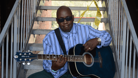 Jesse Boyce seated on steps holding an acoustic guitar
